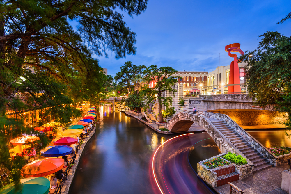 There is an image of downtown San Antonio, TX, with the many attractions and restaurants on the Riverwalk.