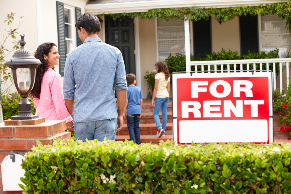 Homeowners standing outside a rental property with a for rent sign after make-ready improvements.